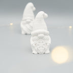 Im Vordergrund steht eine weiße Wichtelfigur aus Gießpulver mit einer großen Schneeflocke in den Händen. Im Hintergrund ist eine weitere, unscharfe Wichtelfigur zu sehen. Der Hintergrund ist hell, einzelne Lichter sorgen für eine sanfte Atmosphäre.