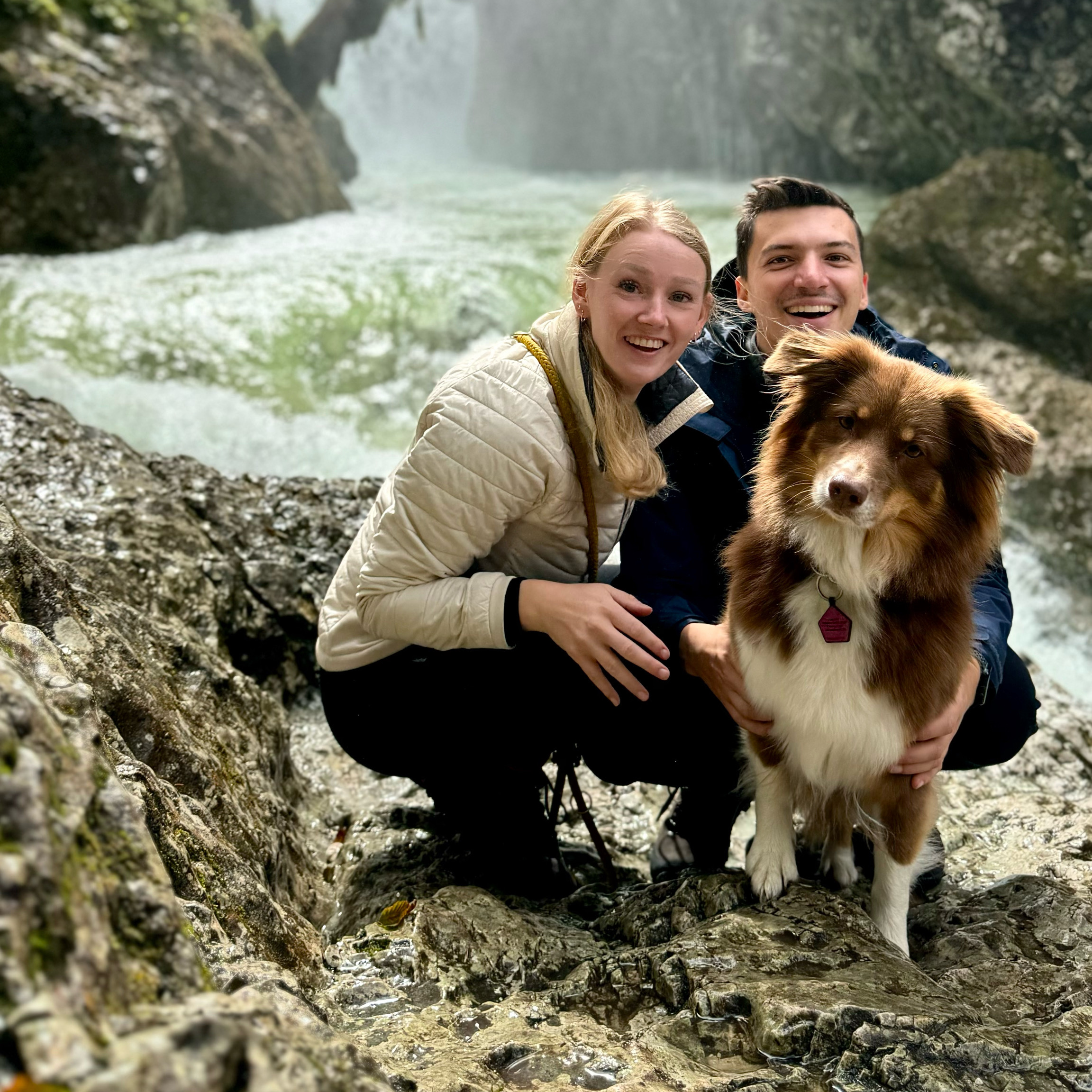 Maike und Anton gemeinsam mit ihrer Hündin Yuna beim Wandern in einer Felslandschaft am Fluss.